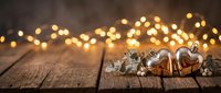 Two golden heart ornaments on rustic wooden surface with eucalyptus sprigs and warm bokeh lights, romantic holiday decor for Valentine or Christmas.