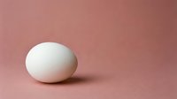 Single white chicken egg on soft pink background with minimal shadow for cooking and food photography concepts.