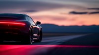Luxury sports car silhouette against dramatic sunset sky, with glowing red taillights illuminating empty road and mountain backdrop.