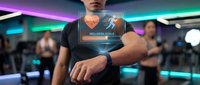 Caucasian male fitness professional displaying holographic wellness data on smartwatch in modern gym with neon lighting and blurred background athletes during workout session.