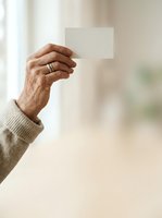 Mature man with dark skin tone holding blank white card in hand wearing beige sweater, ideal for business cards, contact information, and promotional messaging concepts.