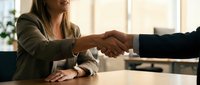 Two professionals shaking hands across a desk in a bright office setting, sealing a business deal or agreement. Suitable for corporate, partnership, and success concepts.