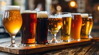 Craft beer flight tasting with various amber, dark and light ales served in different glasses on wooden board in cozy pub atmosphere with warm lighting.