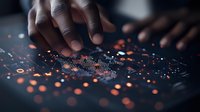African American hands interacting with glowing orange data visualization display on dark surface, showing financial or analytical information in modern technology interface.