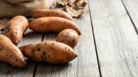 Fresh brown potatoes scattered on rustic wooden surface with burlap fabric, suitable for cooking, recipe, and food photography projects.