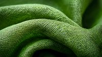 Textured green fabric with soft folds and waves creating abstract curves and shadows, macro photography showing detailed woven textile structure and patterns.