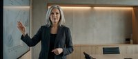 Professional mature businesswoman with gray hair presenting strategy on whiteboard in modern corporate office during meeting.