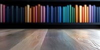 Blurred books on wooden shelf with colorful spines creating rainbow spectrum effect against dark background. Empty wooden table surface in foreground for product display.