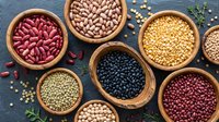 Assorted legumes and beans in wooden bowls including kidney beans, black beans, lentils, and chickpeas arranged on dark slate surface for healthy cooking.