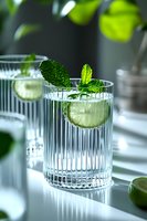Fresh lime and mint cocktail in elegant ribbed glass with natural light. Refreshing summer drink garnished with citrus slice and herbs on reflective surface.