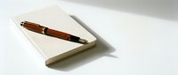 Elegant wooden fountain pen resting on open notebook with blank pages on clean white surface for writing, journaling, and professional correspondence.
