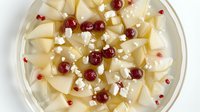 Fresh pear slices arranged on white plate with cranberries and crumbled feta cheese, garnished with pomegranate seeds creating elegant appetizer presentation.