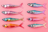 Colorful glitter fish arranged in rows on pink background, shimmering metallic decorative sardines with sparkly tails creating playful marine pattern.
