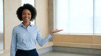 Professional African American businesswoman presenting in modern office space with natural lighting and open palm gesture for corporate presentations.