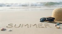 Summer written in sand on a sunny beach with straw hat, sunglasses, and seashells by the ocean waves, evoking vacation and travel.