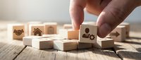 Hand placing wooden cube with paw print among blocks showing pet care symbols on rustic table for veterinary business branding and animal service concepts.
