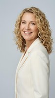 Professional middle-aged Caucasian businesswoman with curly blonde hair smiling confidently in cream blazer against neutral background for corporate use.