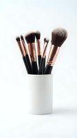 Professional makeup brushes with rose gold ferrules and black handles in white ceramic holder on clean background for beauty and cosmetics applications.
