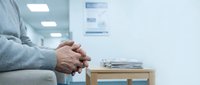 Patient hands clasped while waiting in modern medical clinic examination room for healthcare consultation and treatment.