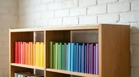 Colorful rainbow books arranged by color in wooden shelf organizer against white brick wall for home library organization and interior design.