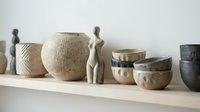 Neutral ceramic and woven vessels arranged on shelf with abstract female figurine, showcasing home decor and interior design styling options.