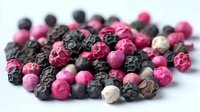Colorful mix of pink, black, and white peppercorns scattered on white surface, adding aromatic spice to gourmet cooking.