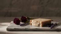 Handmade soap bar with dried rose buds and lavender sprigs on marble board, natural skincare and wellness product for cosmetic and beauty industry use.