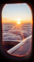Sunrise view from airplane window showing golden sun above clouds with aircraft wing visible, travel and aviation concept for commercial use.