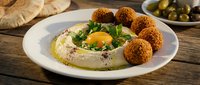 Traditional Middle Eastern hummus plate with crispy falafel balls, fresh herbs, olive oil drizzle and pita bread on rustic wooden table for authentic cuisine.