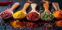 Colorful aromatic spices and dried herbs in wooden spoons on dark background, turmeric, paprika, chili pepper flakes, coriander seeds and sumac powder.