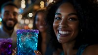 Young Black woman with curly hair smiling while holding glowing blue cocktail at nighttime party with friends and bokeh lights in background.