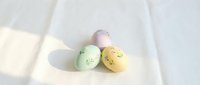 Colorful pastel Easter eggs with cute kawaii faces on soft white fabric with natural sunlight shadows creating minimalist spring holiday decoration.