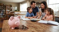 Family budgeting and financial planning with piggy bank and coins on wooden table in modern home kitchen setting with parents teaching children.