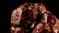 Raw red garnet mineral specimen with crystalline formations and metallic luster on dark background for geology education and gemstone collection displays.