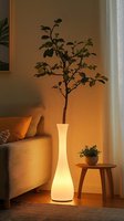 Glowing modern floor vase with green plant branch creating cozy atmosphere in minimalist living room interior with warm ambient lighting and sofa.