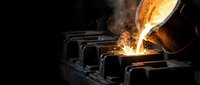 Molten metal being poured from ladle into casting molds in foundry with bright orange glow and sparks flying in industrial metalworking process.
