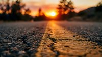 Low angle view of asphalt road with yellow center line at golden hour sunset, suitable for travel, transportation, and journey-themed designs.