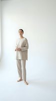 Young Asian woman in beige linen pajamas standing barefoot against white studio background. Minimalist sleepwear fashion portrait for wellness and comfort.