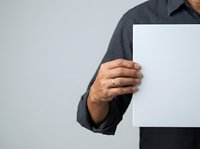 Man in dark gray shirt holding blank white paper or document against neutral background for mockup or presentation purposes.