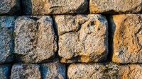 Ancient weathered stone wall with rough textured blocks creating rustic masonry pattern for construction and architectural backgrounds.