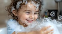 Joyful young girl with curly hair playing with soap bubbles and foam during bath time, laughing with pure happiness and delight in light blue bathroom.