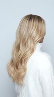 Young Caucasian woman with long wavy blonde hair wearing white sweater against gray background. Hair styling and fashion concept for salon advertising.