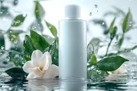 White cosmetic bottle with gardenia flower and green leaves in water splash, droplets floating in air against light background for skincare advertising.
