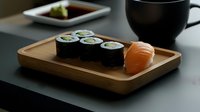 Fresh sushi rolls and salmon nigiri served on wooden plate with dark moody lighting, minimalist Japanese food composition for restaurant menu and food blogs.
