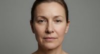 Professional portrait of confident middle-aged Caucasian businesswoman with natural makeup and pulled-back hair against neutral background for corporate use.