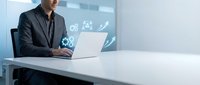 Professional businessman in dark suit working on laptop with digital analytics dashboard displaying growth charts and data visualization in modern office.