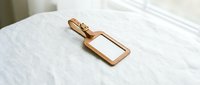 Elegant copper luggage tag with blank nameplate resting on white bedding, perfect for travel accessories and hospitality branding applications.