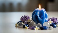 Blue geometric candle burning surrounded by purple flowers, smooth stones and decorative elements creating peaceful spa atmosphere for relaxation and wellness.