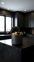 Modern kitchen compost bin with organic waste on dark countertop in contemporary home interior with black cabinets and natural lighting for sustainable living.