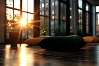 Soft cushions on wooden floor at sunset with golden sunlight streaming through large windows, creating warm atmospheric mood in modern interior space.